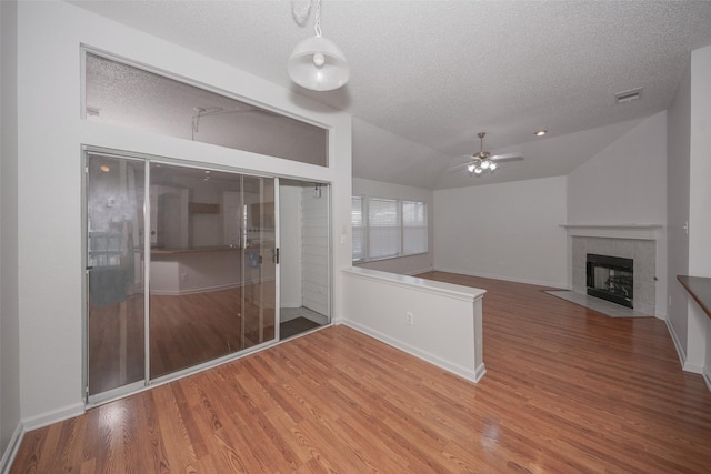 unfurnished living room featuring hardwood / wood-style floors, vaulted ceiling, ceiling fan, a fireplace, and a textured ceiling