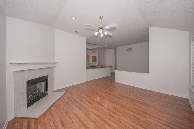 unfurnished living room with ceiling fan, a fireplace, a textured ceiling, and light wood-type flooring