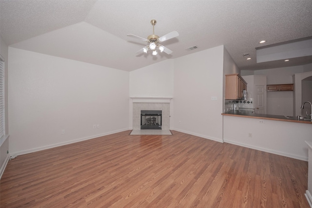 unfurnished living room with lofted ceiling, a tile fireplace, hardwood / wood-style flooring, ceiling fan, and a textured ceiling