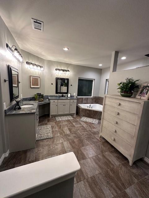 bathroom featuring a relaxing tiled tub and vanity