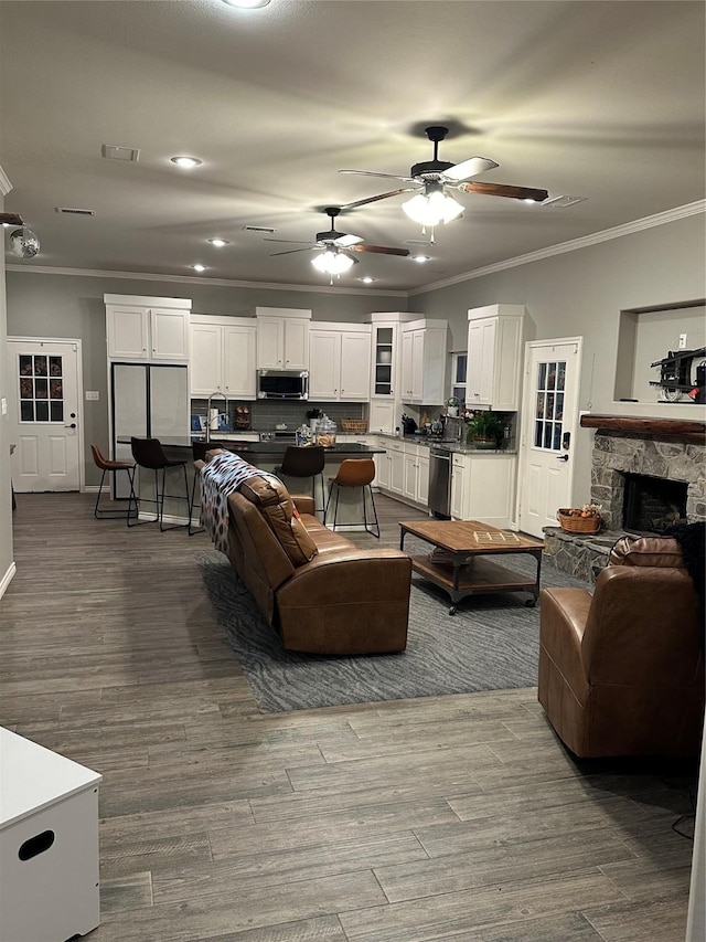 living room with a stone fireplace, ceiling fan, and ornamental molding