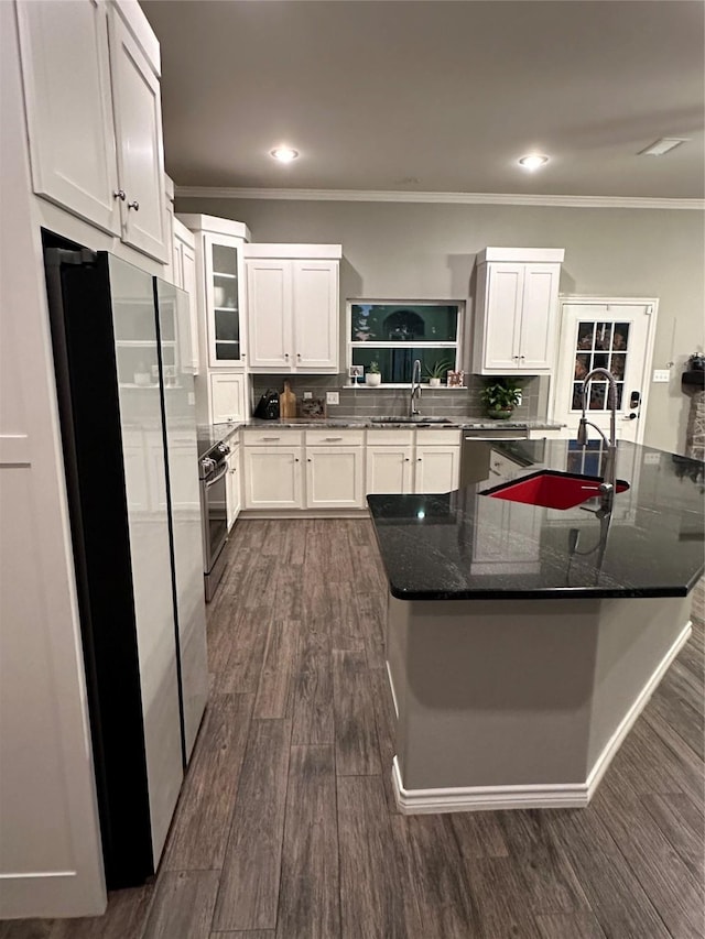 kitchen with dark wood-type flooring, crown molding, appliances with stainless steel finishes, dark stone counters, and white cabinets