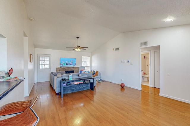 living room featuring lofted ceiling, ceiling fan, light hardwood / wood-style floors, a textured ceiling, and a brick fireplace