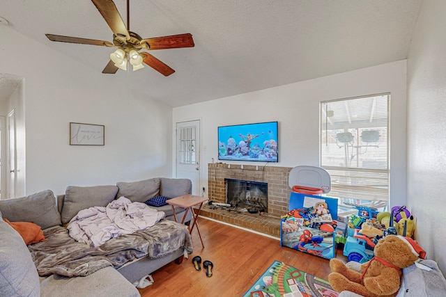 living room with a textured ceiling, hardwood / wood-style flooring, a brick fireplace, and ceiling fan