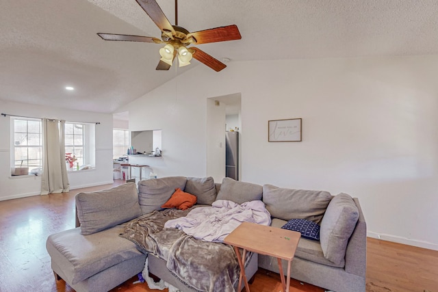 living room with a textured ceiling, light hardwood / wood-style flooring, ceiling fan, and lofted ceiling