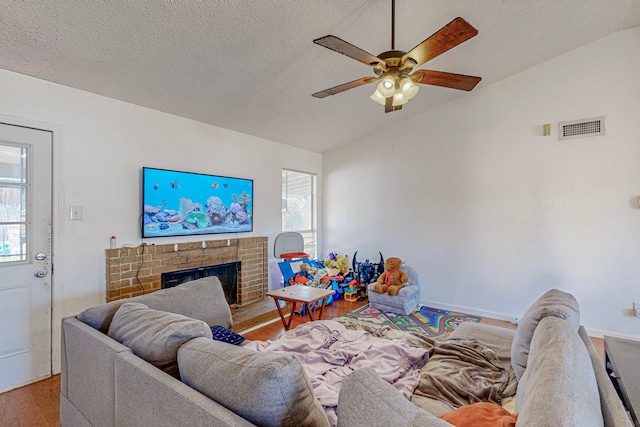 living room with a fireplace, ceiling fan, light hardwood / wood-style flooring, and a textured ceiling