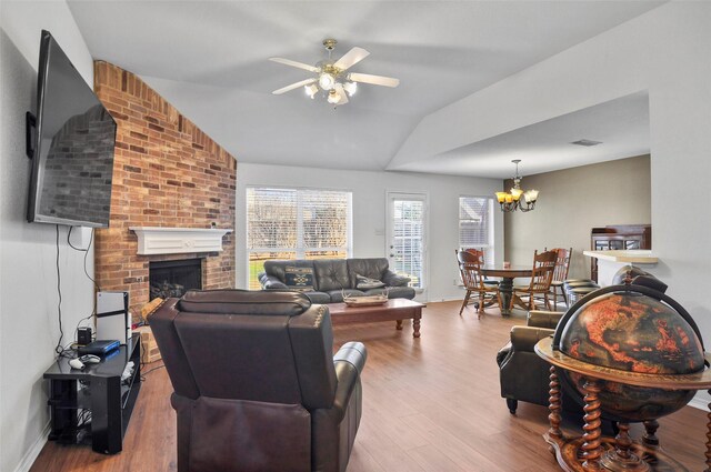 living room with a brick fireplace, ceiling fan with notable chandelier, light hardwood / wood-style floors, and vaulted ceiling