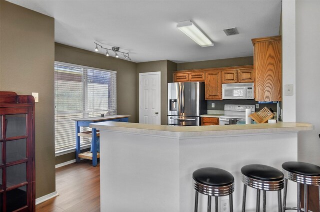 kitchen with kitchen peninsula, a breakfast bar, wood-type flooring, and white appliances