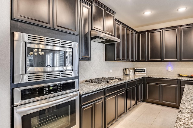 kitchen featuring light stone countertops, light tile patterned floors, tasteful backsplash, a notable chandelier, and stainless steel appliances