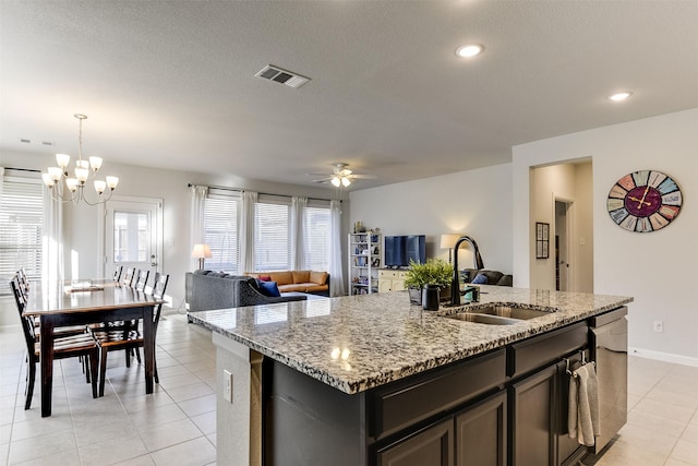 kitchen featuring a kitchen island with sink, hanging light fixtures, sink, stainless steel dishwasher, and light stone countertops