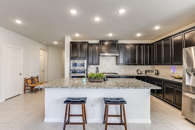 kitchen featuring a center island, backsplash, light tile patterned floors, light stone countertops, and appliances with stainless steel finishes