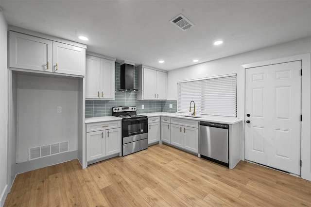 kitchen with sink, stainless steel appliances, wall chimney range hood, tasteful backsplash, and white cabinets