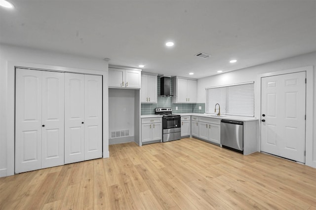 kitchen with white cabinetry, stainless steel appliances, wall chimney range hood, tasteful backsplash, and light hardwood / wood-style flooring