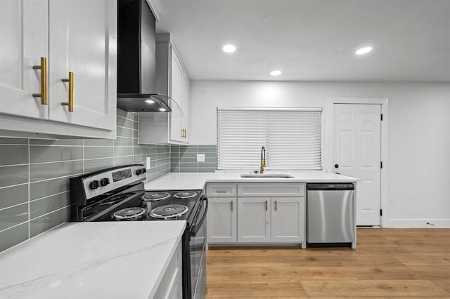 kitchen featuring white cabinets, wall chimney range hood, sink, light wood-type flooring, and stainless steel appliances