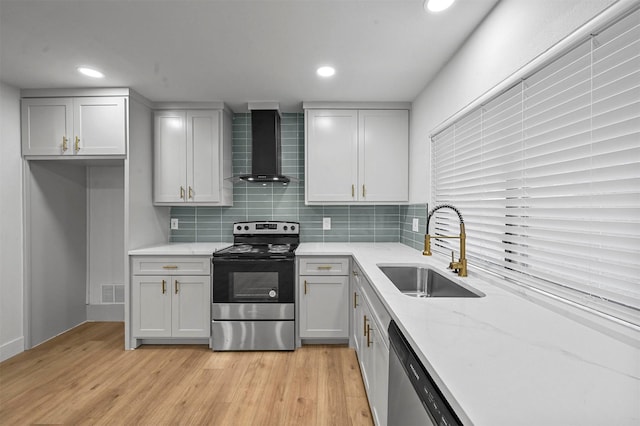 kitchen featuring wall chimney range hood, sink, decorative backsplash, appliances with stainless steel finishes, and light hardwood / wood-style floors