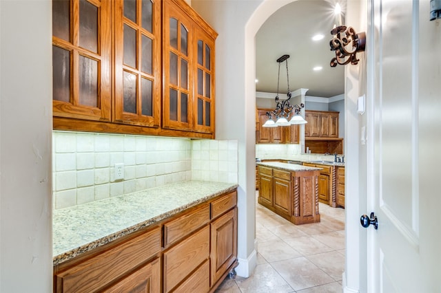 kitchen featuring light stone counters, tasteful backsplash, hanging light fixtures, light tile patterned floors, and ornamental molding