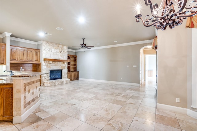 unfurnished living room featuring sink, crown molding, a fireplace, light tile patterned flooring, and ceiling fan with notable chandelier