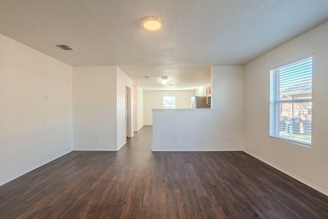 empty room featuring dark wood-type flooring, plenty of natural light, and a textured ceiling