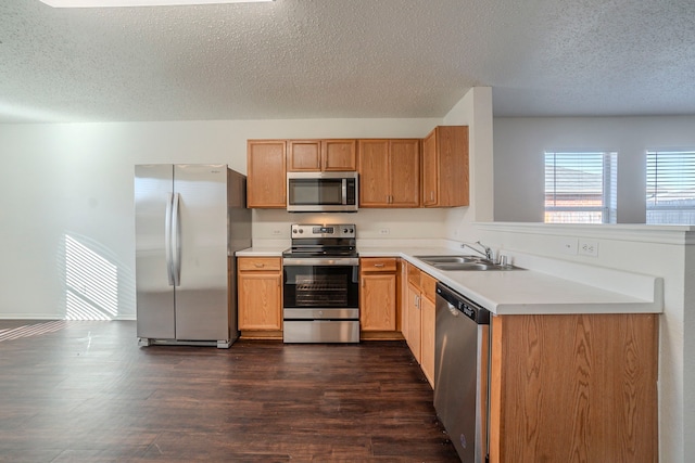 kitchen with appliances with stainless steel finishes, sink, dark wood-type flooring, and kitchen peninsula