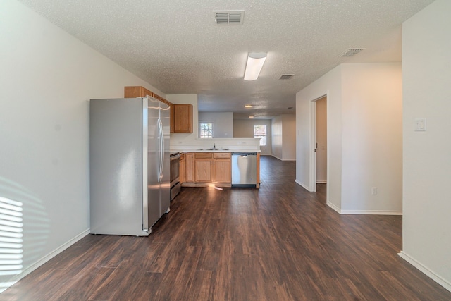 kitchen with sink, a textured ceiling, dark hardwood / wood-style floors, kitchen peninsula, and stainless steel appliances