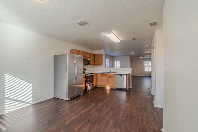 kitchen with appliances with stainless steel finishes, dark hardwood / wood-style floors, sink, kitchen peninsula, and a textured ceiling