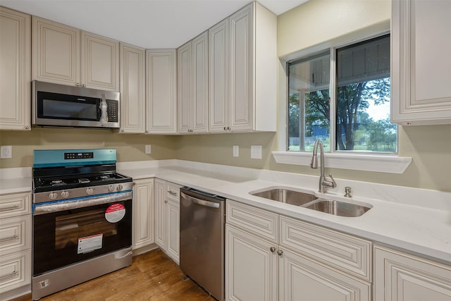 kitchen with light stone countertops, light wood-type flooring, sink, and appliances with stainless steel finishes