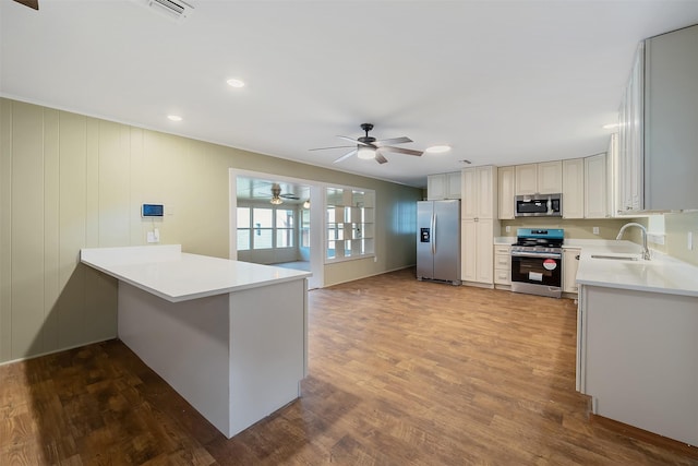 kitchen with kitchen peninsula, stainless steel appliances, ceiling fan, dark wood-type flooring, and sink