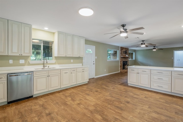 kitchen with stainless steel dishwasher, ceiling fan, sink, a fireplace, and light hardwood / wood-style floors