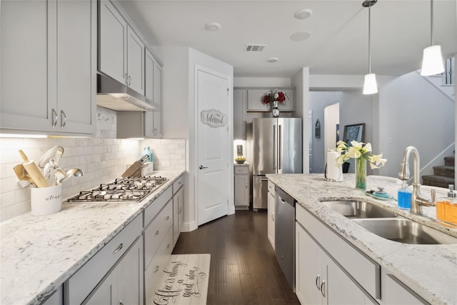 kitchen with hanging light fixtures, sink, appliances with stainless steel finishes, tasteful backsplash, and light stone counters