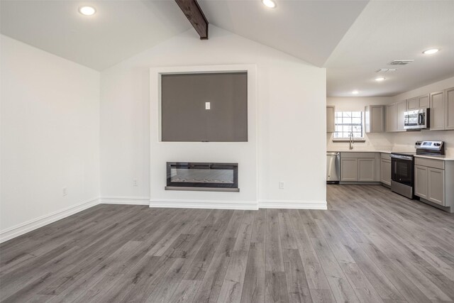 unfurnished living room featuring lofted ceiling with beams, light wood-type flooring, and sink