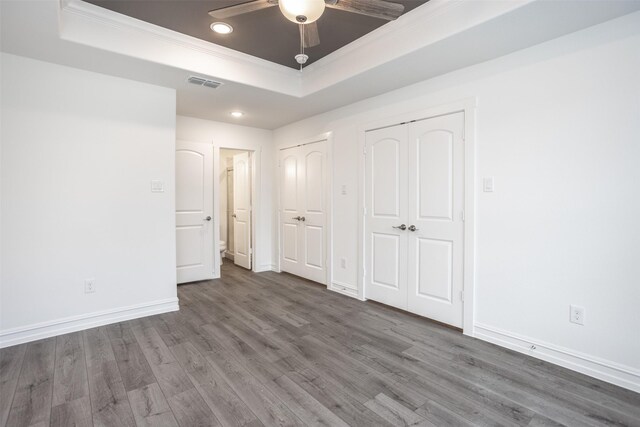 unfurnished bedroom with ceiling fan, dark hardwood / wood-style flooring, ornamental molding, and a tray ceiling