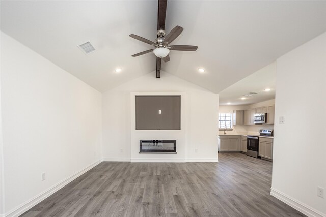 unfurnished living room featuring ceiling fan, hardwood / wood-style floors, lofted ceiling with beams, and sink