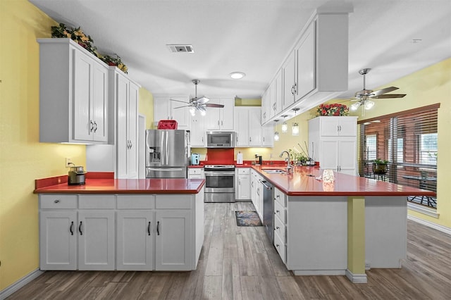 kitchen with sink, kitchen peninsula, wood-type flooring, white cabinets, and appliances with stainless steel finishes