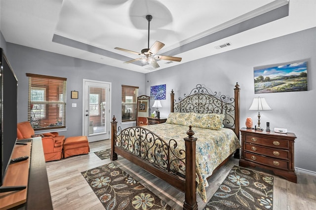 bedroom with hardwood / wood-style floors, a raised ceiling, crown molding, ceiling fan, and access to exterior