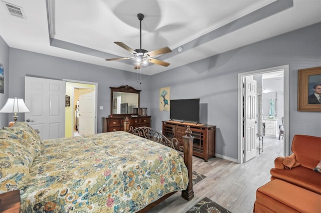 bedroom with ornamental molding, a raised ceiling, ceiling fan, light hardwood / wood-style flooring, and connected bathroom