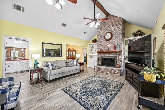 living room with ceiling fan, sink, a brick fireplace, lofted ceiling with beams, and light hardwood / wood-style floors