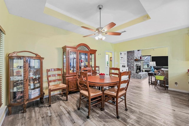 dining area with hardwood / wood-style floors, a raised ceiling, and a stone fireplace