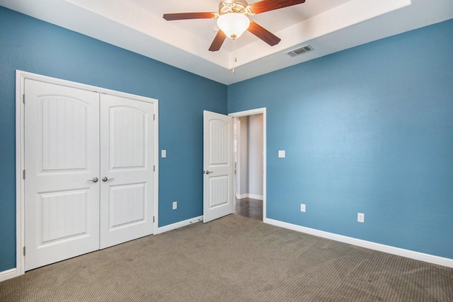 unfurnished bedroom with ceiling fan, light carpet, a tray ceiling, and a closet