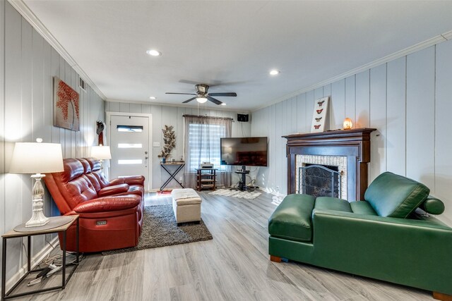 living room featuring a fireplace, ceiling fan, crown molding, and light hardwood / wood-style flooring