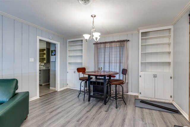 dining area with light wood-type flooring, built in features, crown molding, and a notable chandelier