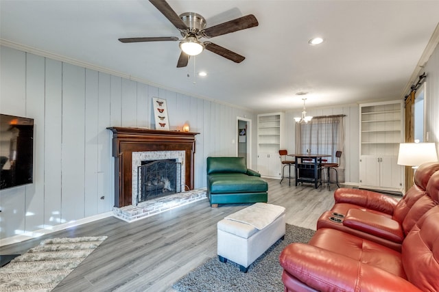 living room with built in shelves, light hardwood / wood-style floors, ceiling fan with notable chandelier, and ornamental molding