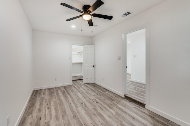 unfurnished bedroom featuring light wood-type flooring, a closet, a spacious closet, and ceiling fan