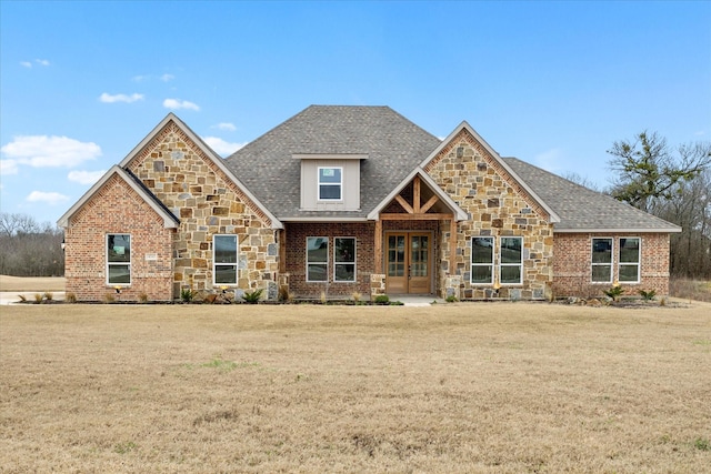 craftsman house featuring roof with shingles, french doors, brick siding, stone siding, and a front lawn