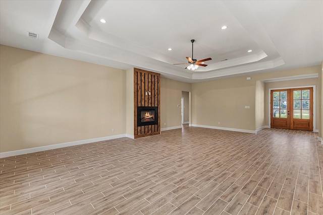 unfurnished living room featuring a tray ceiling, light wood finished floors, baseboards, and ceiling fan