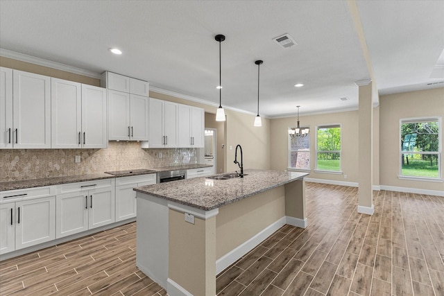 kitchen featuring baseboards, light wood finished floors, visible vents, a sink, and backsplash