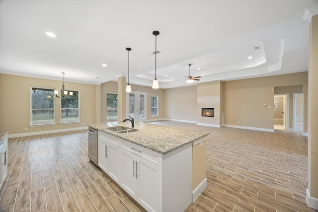 kitchen featuring a sink, light wood-style flooring, baseboards, and a tray ceiling