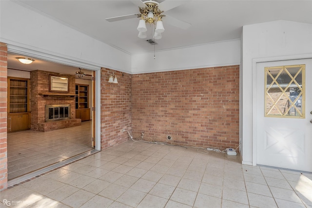 empty room featuring ceiling fan, brick wall, and a brick fireplace