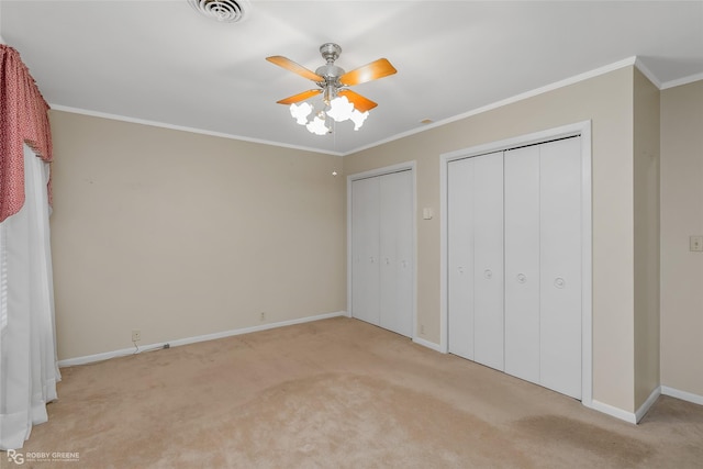 unfurnished bedroom with ceiling fan, light colored carpet, ornamental molding, and two closets