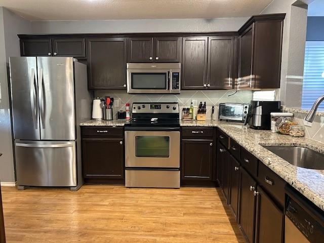 kitchen with light wood-style floors, light stone counters, stainless steel appliances, and a sink