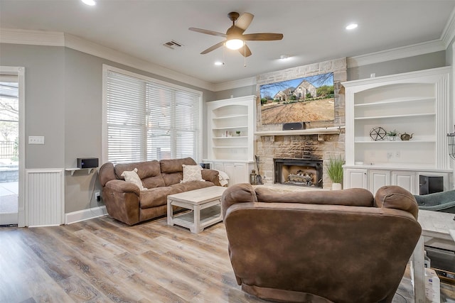 living room with light hardwood / wood-style floors, crown molding, ceiling fan, a fireplace, and built in shelves